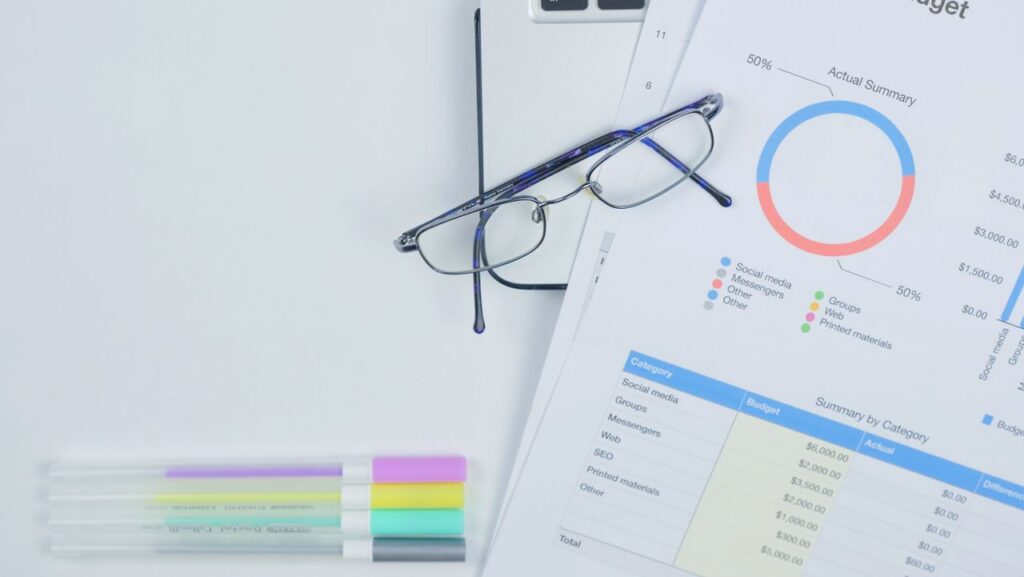 A modern workspace featuring budget graph, laptop, glasses, and stationery for creative business planning.